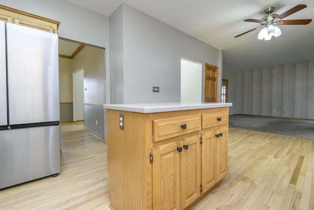 kitchen featuring a ceiling fan, light wood-style flooring, a kitchen island, freestanding refrigerator, and light countertops