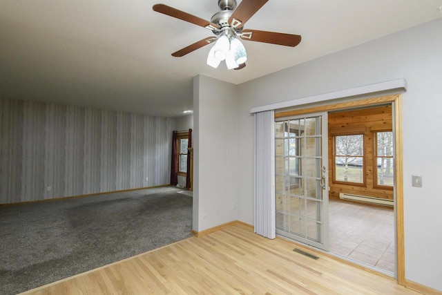 spare room with a baseboard radiator, wood finished floors, a ceiling fan, visible vents, and baseboards