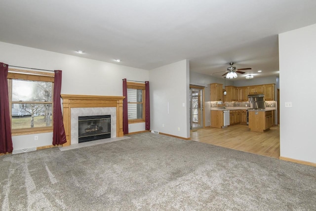 unfurnished living room featuring a healthy amount of sunlight, baseboards, a tiled fireplace, and light colored carpet