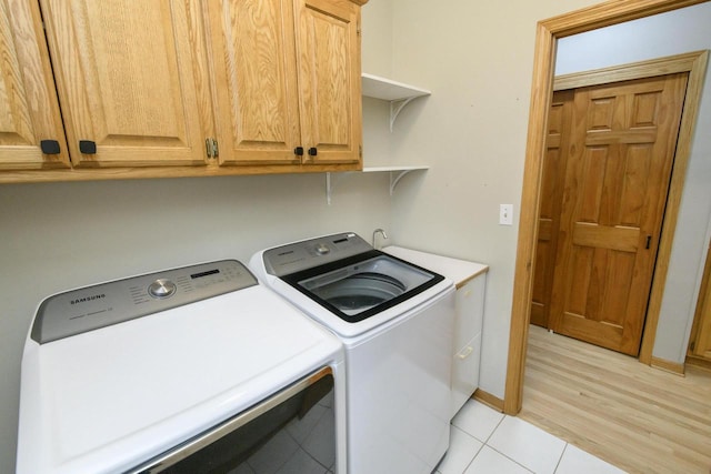 washroom featuring separate washer and dryer, light wood-style flooring, cabinet space, and baseboards