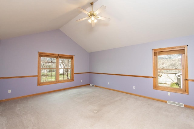 carpeted empty room with a ceiling fan, visible vents, vaulted ceiling, and baseboards