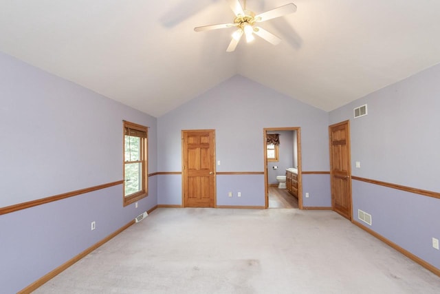 empty room with light colored carpet, visible vents, vaulted ceiling, and baseboards