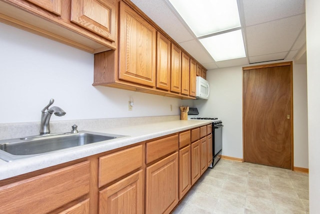 kitchen featuring white microwave, light countertops, a paneled ceiling, a sink, and gas stove