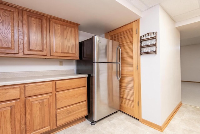 kitchen featuring brown cabinets, freestanding refrigerator, light countertops, and baseboards