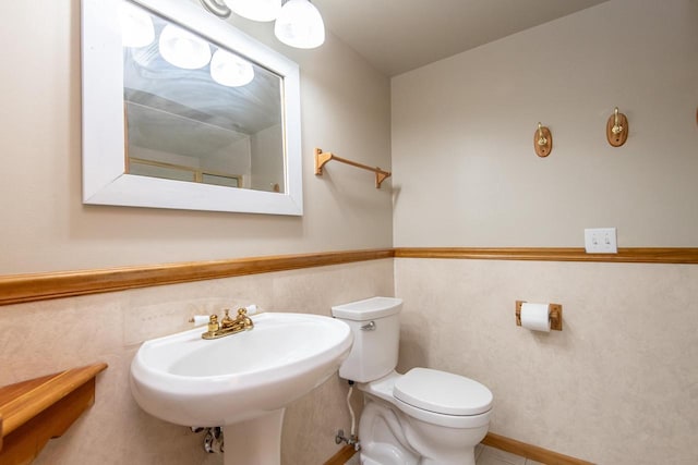 half bathroom featuring toilet, a wainscoted wall, tile patterned flooring, and a sink