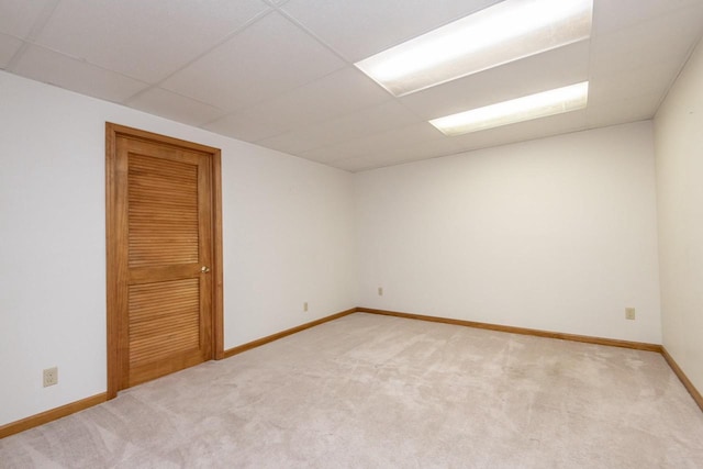 empty room with baseboards, a paneled ceiling, and light colored carpet