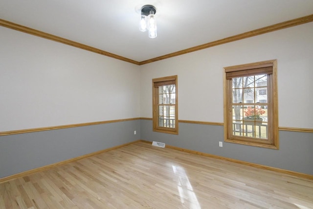 empty room with ornamental molding, wood finished floors, visible vents, and baseboards