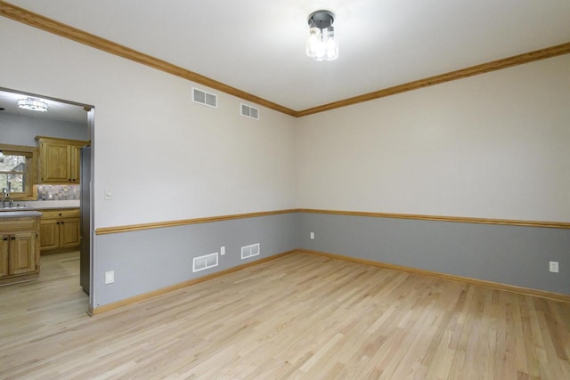 empty room with visible vents, crown molding, and light wood finished floors