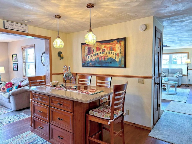 kitchen featuring a center island, decorative light fixtures, brown cabinets, dark wood-type flooring, and open floor plan