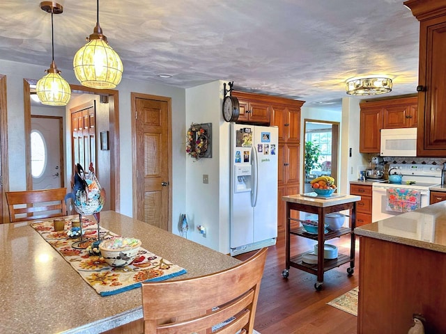 kitchen with white appliances, dark wood-type flooring, hanging light fixtures, light countertops, and tasteful backsplash