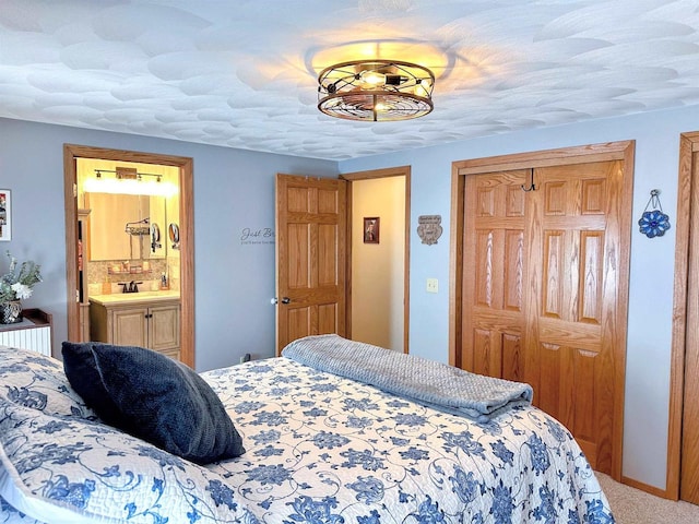 carpeted bedroom featuring a textured ceiling, ensuite bath, a closet, and a sink