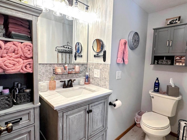 bathroom featuring toilet, baseboards, vanity, and decorative backsplash