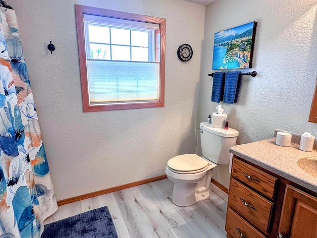 bathroom featuring a textured wall, toilet, wood finished floors, vanity, and baseboards