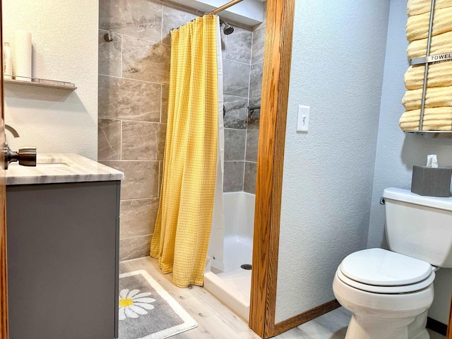 full bathroom with a textured wall, toilet, wood finished floors, vanity, and a shower stall