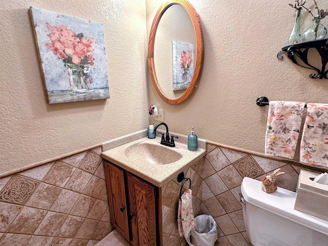 half bathroom with toilet, vanity, tile walls, and a textured wall