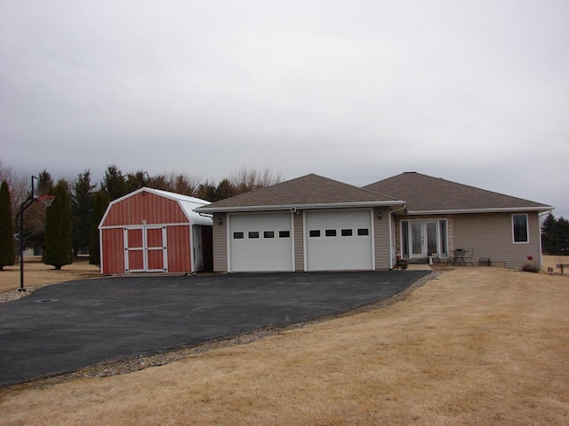 view of front facade with a garage, aphalt driveway, an outbuilding, a shed, and a front yard