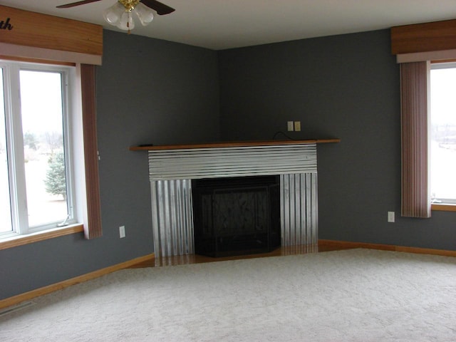 unfurnished living room with a healthy amount of sunlight, carpet floors, baseboards, and a glass covered fireplace