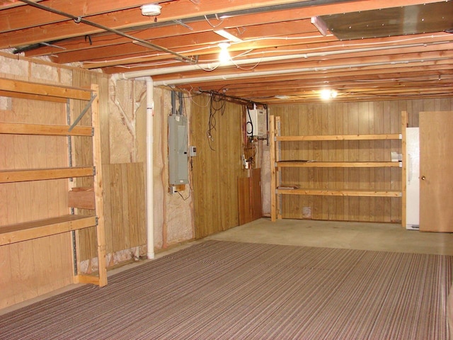 unfinished basement featuring wooden walls, electric panel, and carpet flooring