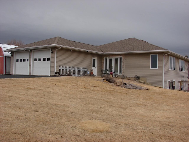 ranch-style home featuring aphalt driveway, an attached garage, french doors, roof with shingles, and a front yard