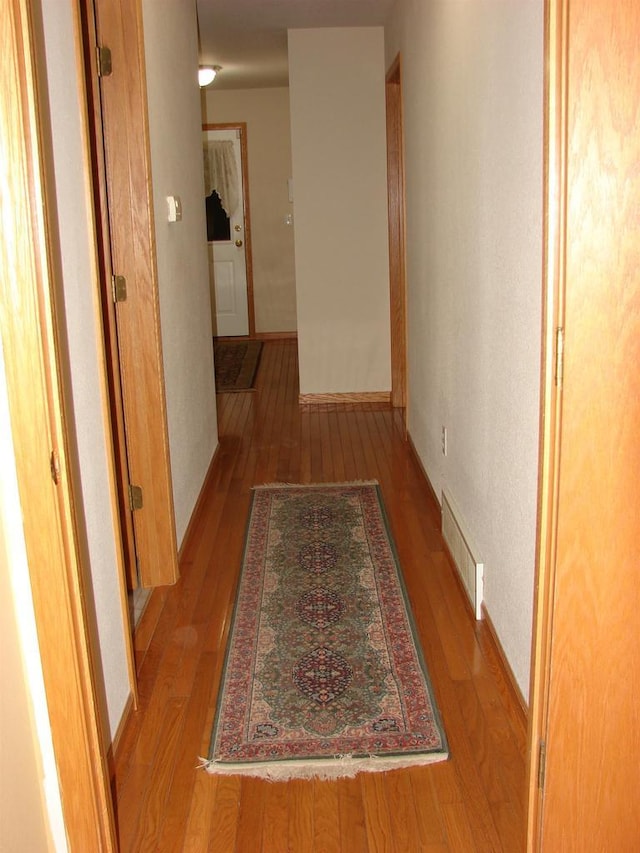 corridor featuring wood-type flooring, visible vents, and baseboards