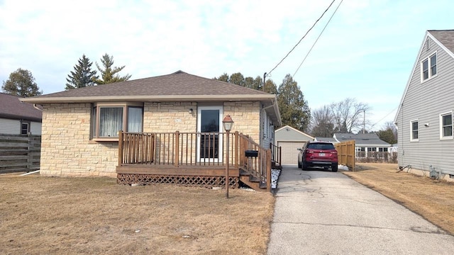 view of front of home with an outbuilding, a shingled roof, fence, driveway, and stone siding