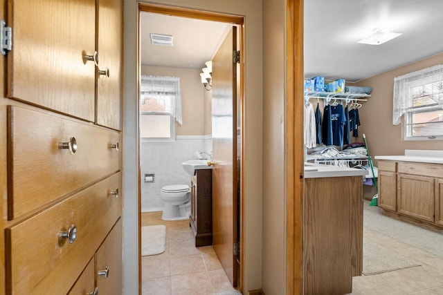 bathroom with toilet, a wainscoted wall, visible vents, tile walls, and tile patterned floors