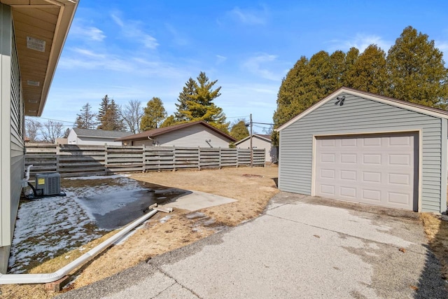 view of yard featuring concrete driveway, a detached garage, fence, an outdoor structure, and central AC