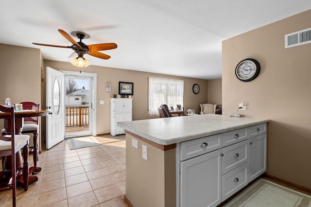 kitchen featuring light tile patterned floors, light countertops, visible vents, a peninsula, and baseboards