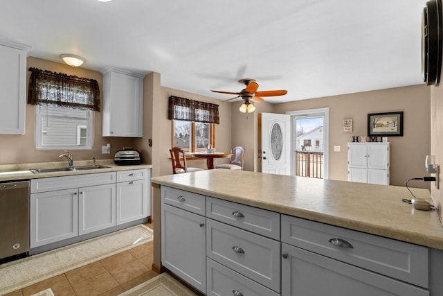 kitchen with light tile patterned flooring, a sink, light countertops, stainless steel dishwasher, and a wealth of natural light