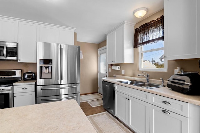 kitchen with light countertops, appliances with stainless steel finishes, white cabinetry, a sink, and baseboards