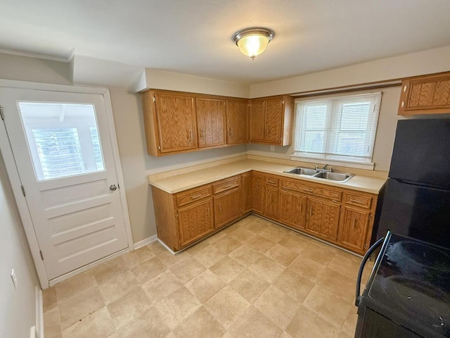 kitchen with freestanding refrigerator, brown cabinets, a sink, and stove