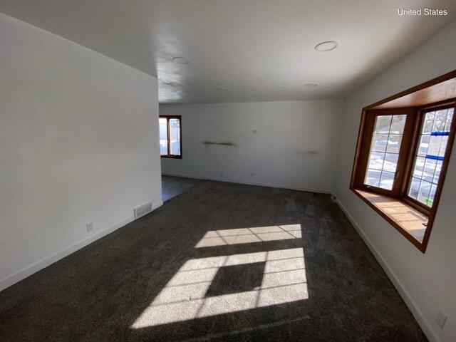 spare room with dark colored carpet, visible vents, and baseboards