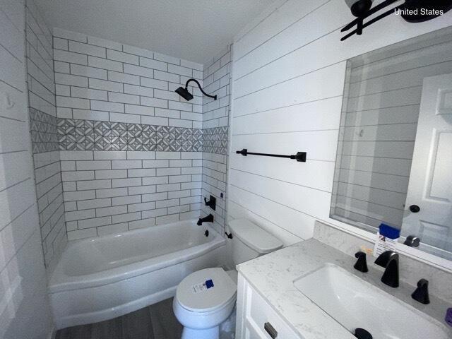 bathroom featuring toilet, wooden walls, bathtub / shower combination, and vanity