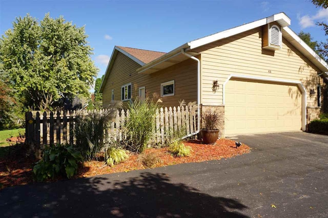 view of home's exterior featuring a garage, stone siding, driveway, and fence