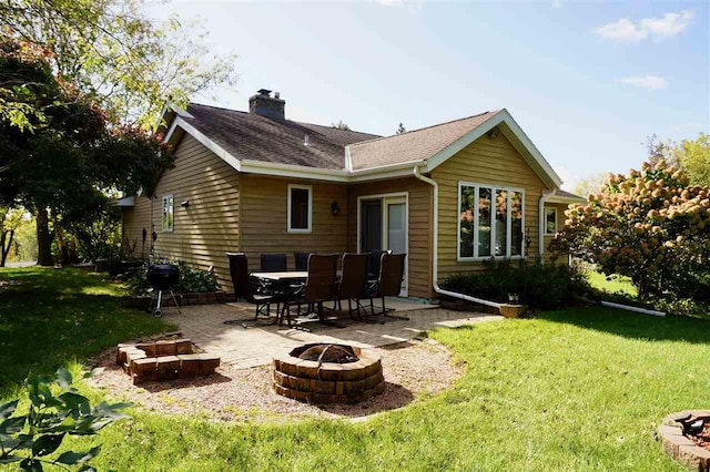 rear view of property featuring a patio, roof with shingles, a yard, a chimney, and a fire pit