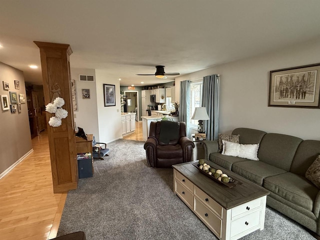 living room featuring light wood-style floors, baseboards, visible vents, and ceiling fan