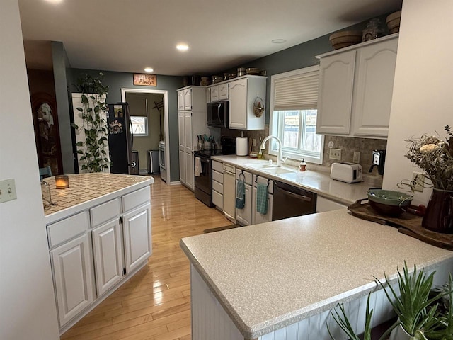 kitchen featuring a peninsula, a sink, decorative backsplash, black appliances, and light countertops