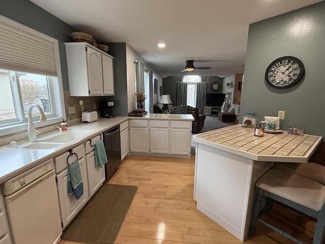 kitchen featuring a peninsula, white dishwasher, a sink, tile counters, and black dishwasher