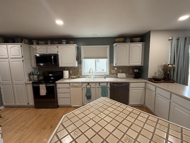 kitchen featuring black microwave, dishwashing machine, electric stove, white cabinetry, and a sink