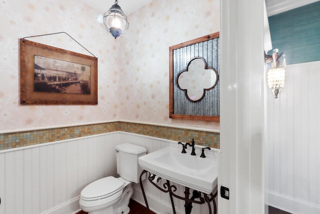 bathroom featuring a wainscoted wall, toilet, and wallpapered walls