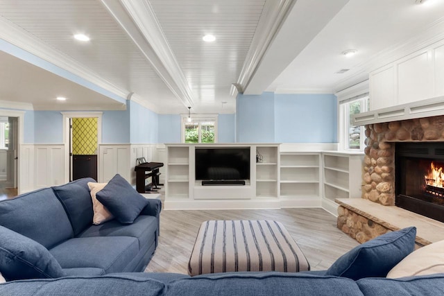 living area featuring wainscoting, ornamental molding, light wood-style floors, and a stone fireplace