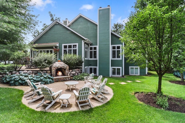 back of property with an outdoor stone fireplace, a patio area, a lawn, and a chimney