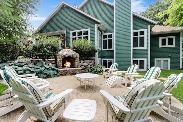 back of property featuring a chimney, an outdoor stone fireplace, and a patio area