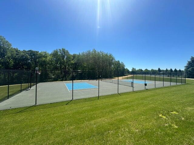 view of basketball court with a tennis court, fence, and a lawn