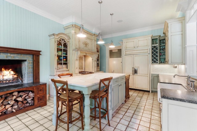 kitchen featuring a fireplace, a kitchen island, paneled built in fridge, ornamental molding, and decorative light fixtures