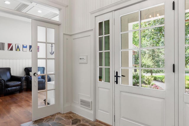 entryway featuring a wainscoted wall, stone finish flooring, visible vents, and french doors