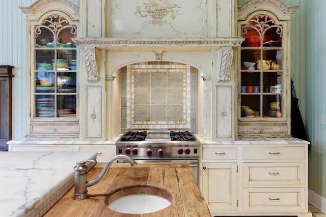 kitchen with light stone countertops, cream cabinets, a sink, and stainless steel stove