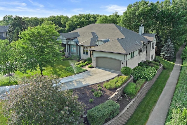 view of front of home featuring roof with shingles, a chimney, concrete driveway, an attached garage, and a front lawn