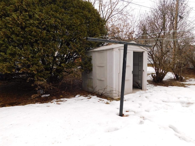 snow covered structure featuring an outbuilding and a shed