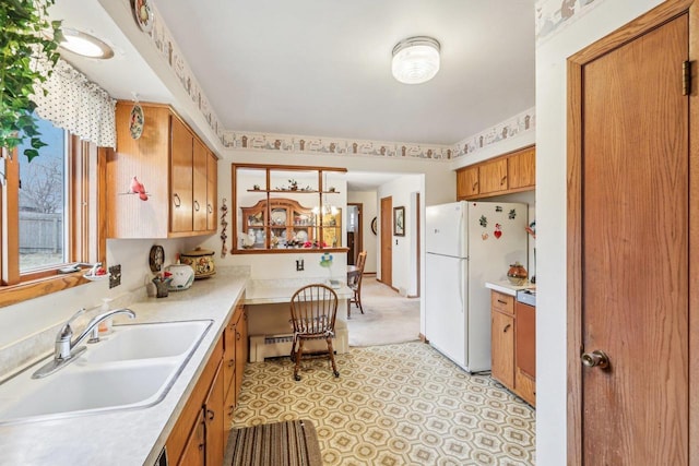 kitchen featuring brown cabinets, freestanding refrigerator, a sink, light countertops, and built in desk